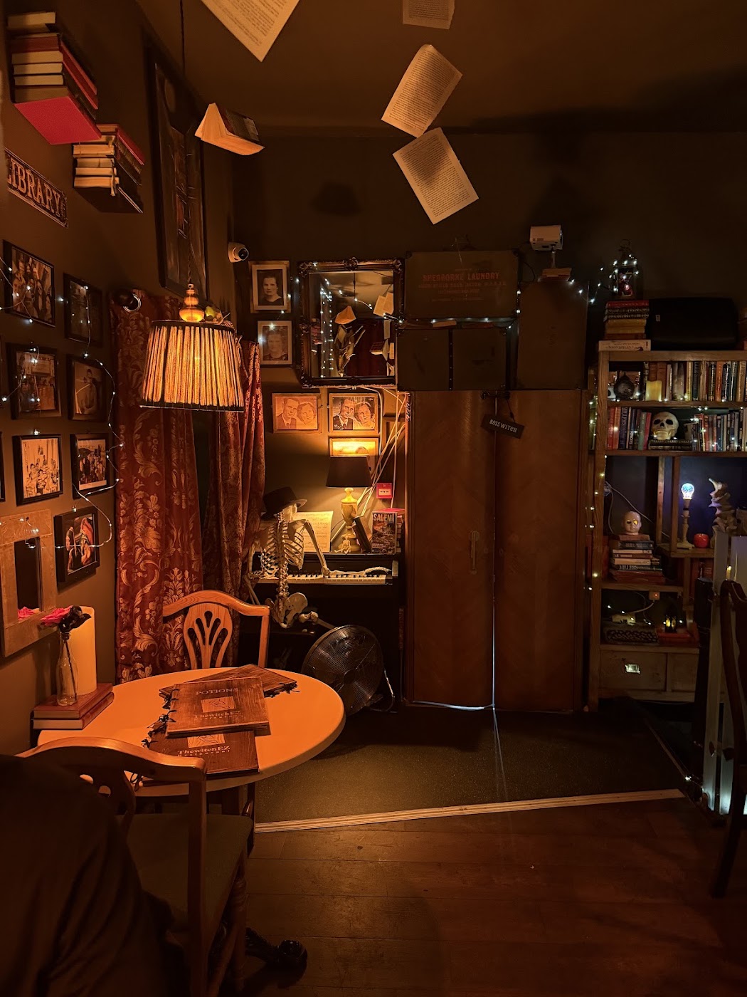 Wall of framed vintage portraits above candles, books and a witch figurine at ThewitchEZ